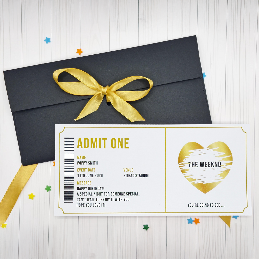 Black envelope with gold ribbon and concert ticket design on a light wooden surface